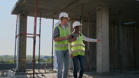 Supervisor-of-a-building-under-construction-man-discussing-with-engineer-designer-woman-the-progress-of-construction-and-examines-a-building-plan.
